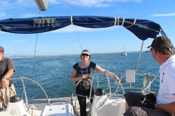 Seglerin steht am Steuerrad, im Hintergrund blaues Wasser und Inselwelt