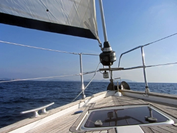 Blick vom Bug einer Segelyacht, vorne blaues Wasser und Himmel, weiter hinten verschwommen eine Insel